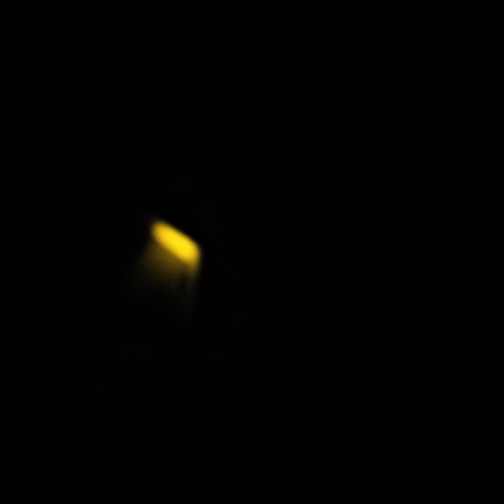 Dark, low-key photograph of a circuit board in deep shadow, near-black surface with a faint amber reflection on copper traces.